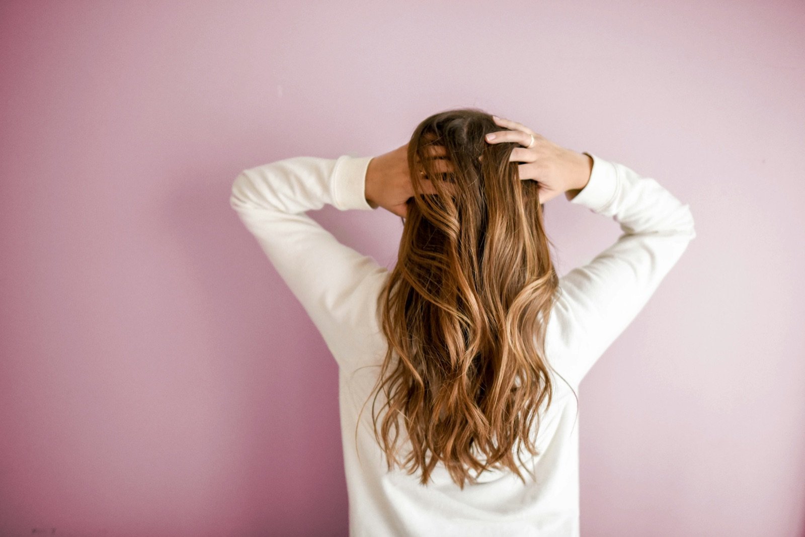 Woman seen from behind holding her long hair with both hands